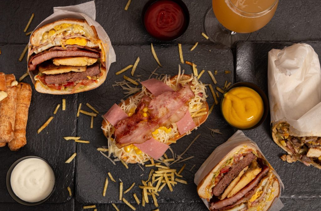 Sandwiches, burgers, burritos fried rolls and various sauces on the black surface